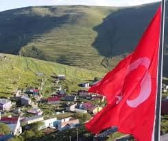 Türk bayrağının arkasındaki köy ve yamaçta görülen Atatürk silüeti